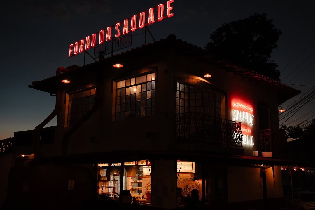 Fachada do Forno da Saudade à noite, com letreiro neon vermelho no telhado