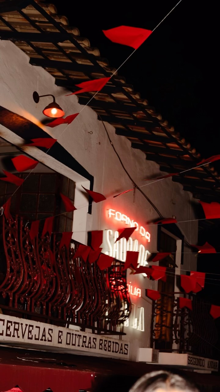 Fachada do Forno da Saudade à noite com bandeirinhas vermelhas de festa